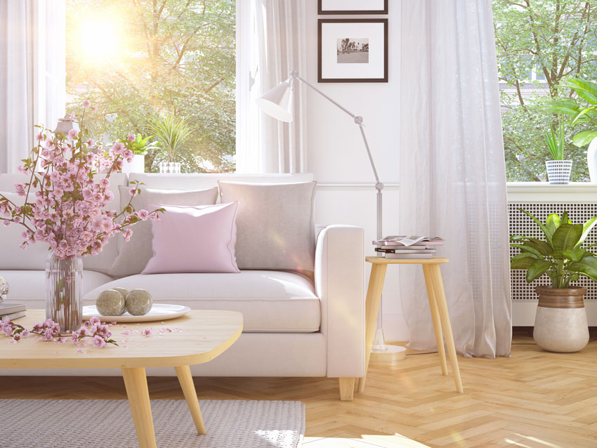 Canapé blanc avec coussin rose, table basse en bois avec vase à fleurs printanier.