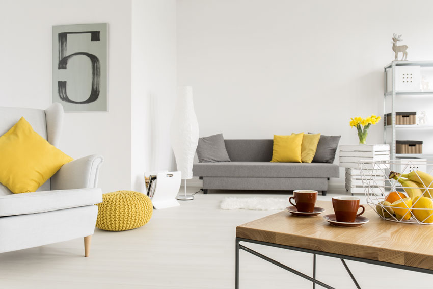 Salon blanc avec coussins jaunes, table basse en bois avec fruits.