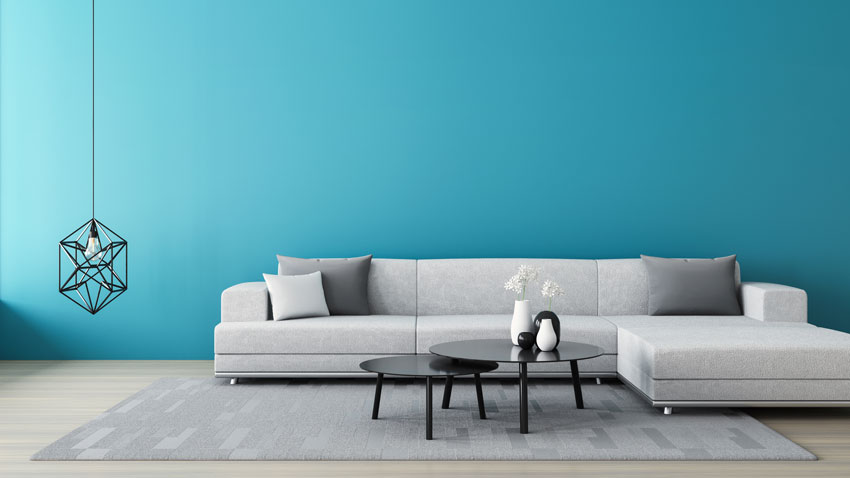 Salon avec canapé d'angle gris et mur bleu clair, lampadaire suspendu style vintage.