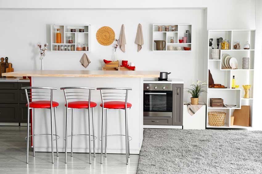 Cuisine moderne blanche avec tabouret et accessoires décoratifs rouges.