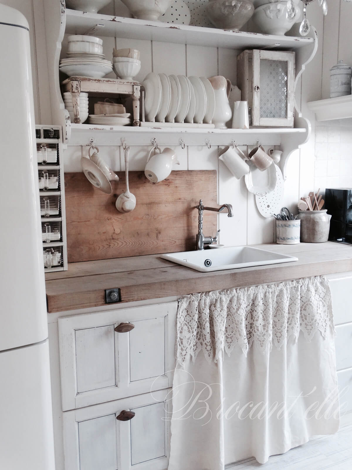 Cuisine style country avec étagères en bois et petit rideau sous lavabo.