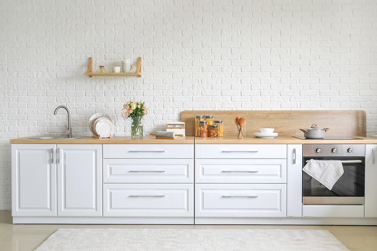 Cuisine blanche moderne avec plan de travail en bois et revêtement mural en briques blanches.