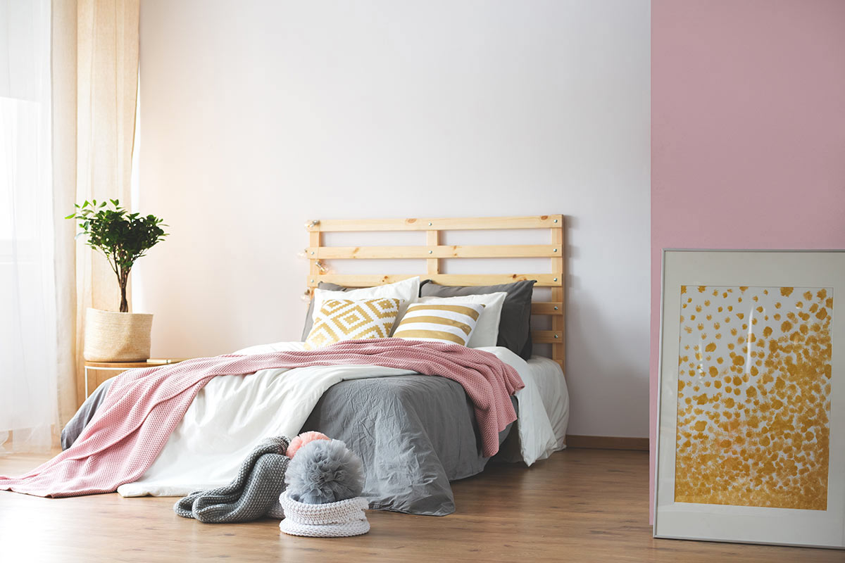Tête de lit DIY en palettes dans cette chambre au mur blanc et rose.