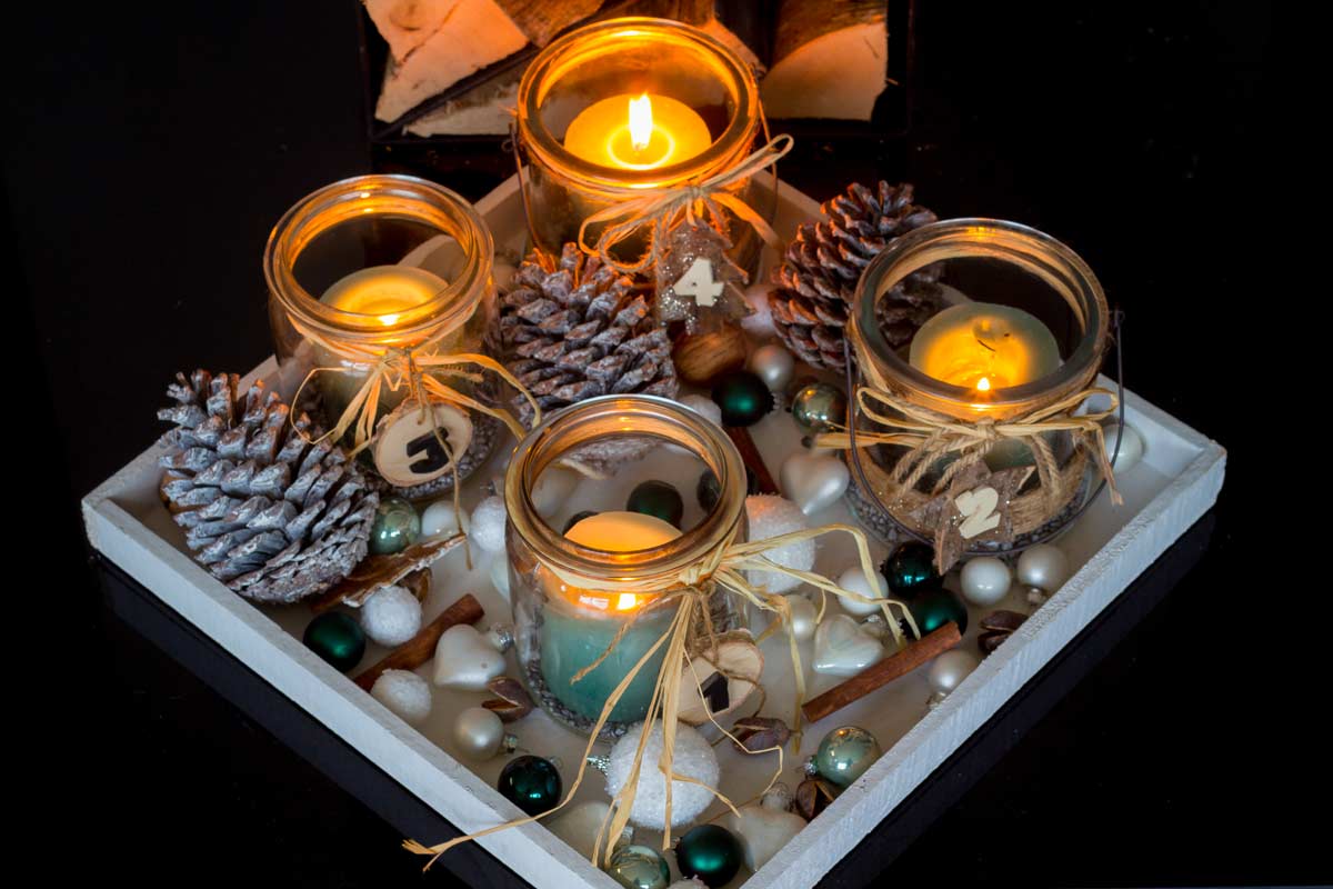 Ensemble de bougies placées dans des bocaux en verre, accompagnées de pommes de pin et décorées de chiffres. Les bocaux en verre agissent comme des lanternes.