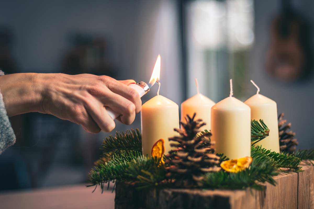 L'action de l'allumage d'une bougie entourée de pommes de pin et de branches de sapin, illustrant la préparation d'un centre de table chaleureux.