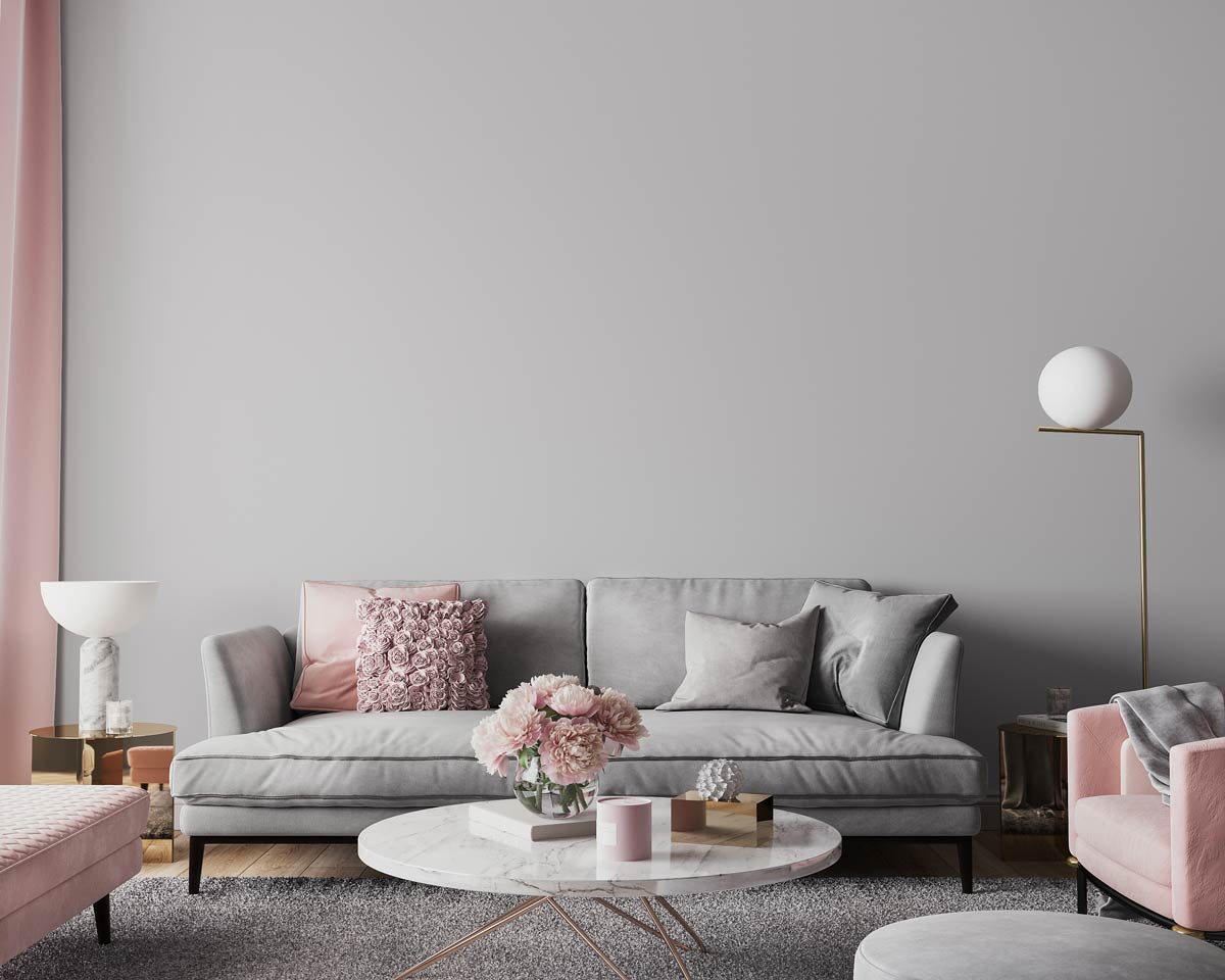 Salon avec mur et canapé gris avec coussins roses.
